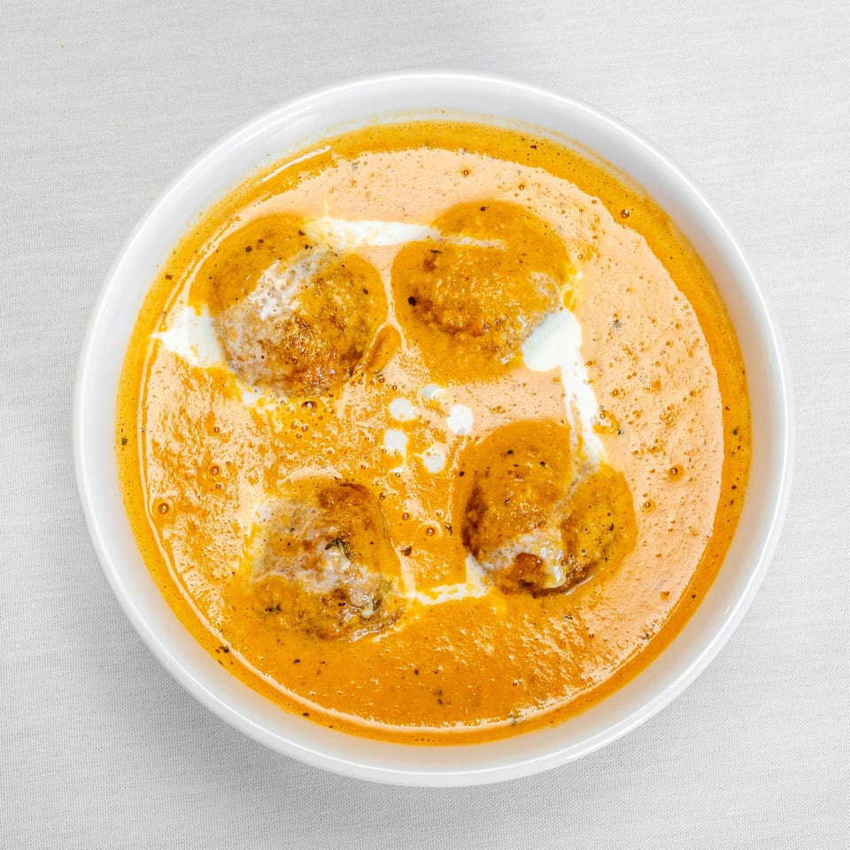 Overhead view of browned dumplings in creamy orange curry sauce, drizzled with white cream, served in a white bowl.