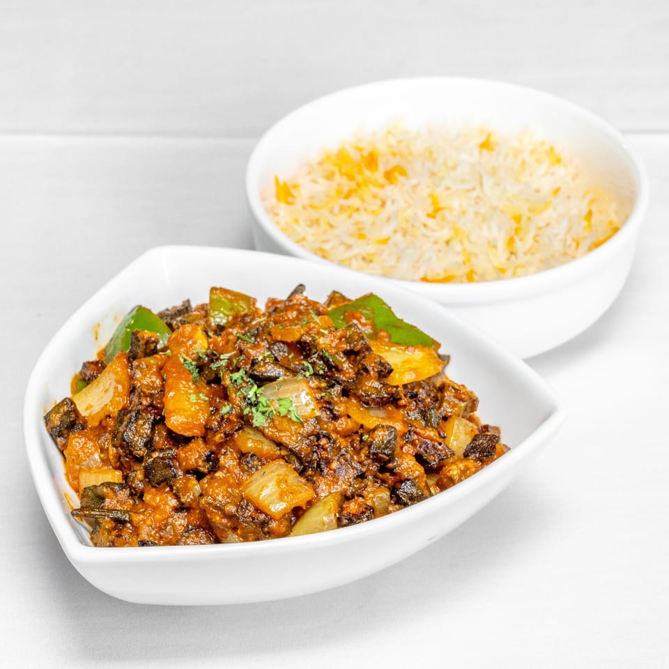 Spicy sautéed vegetables with peppers and onions served in a white dish alongside a bowl of seasoned rice.