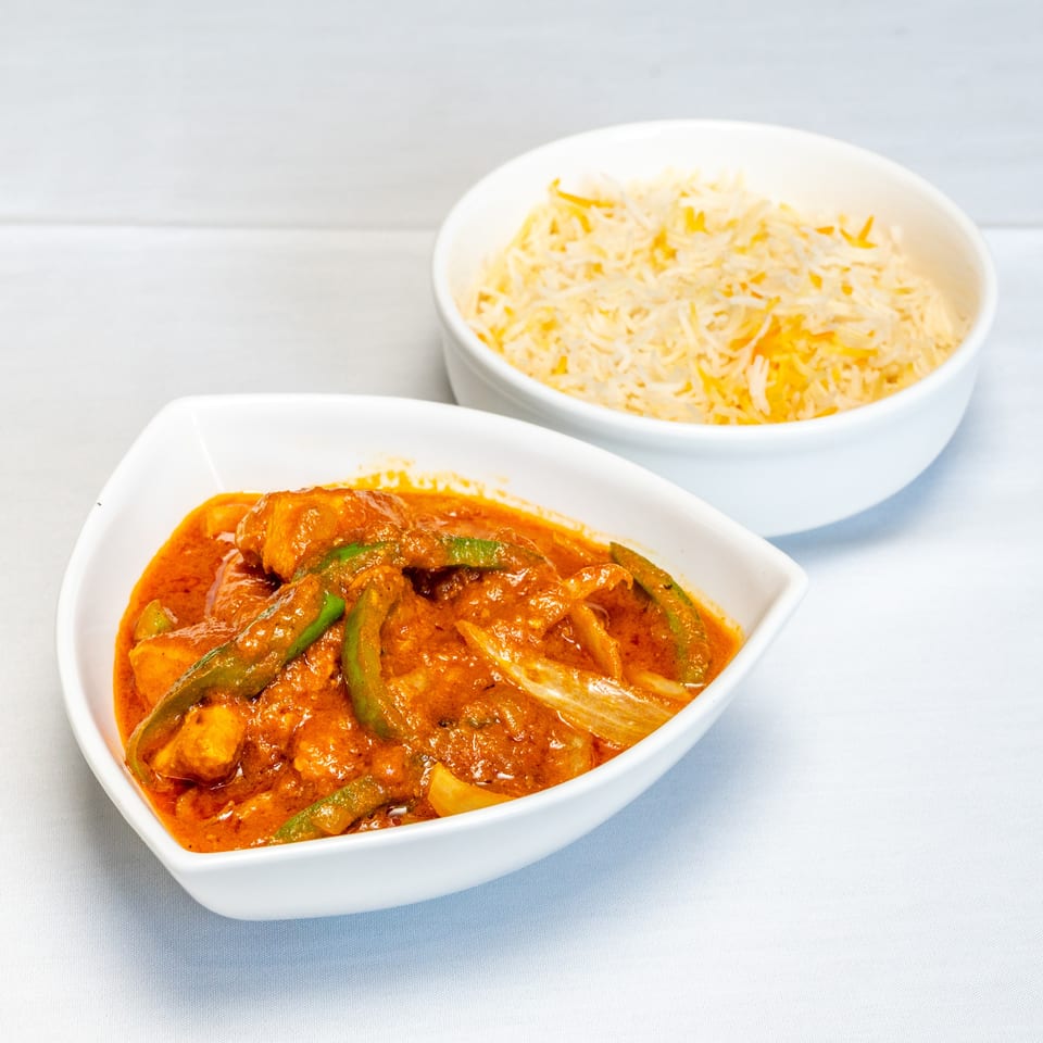 Creamy orange chicken curry with green peppers and onions served alongside basmati rice in white dishes.