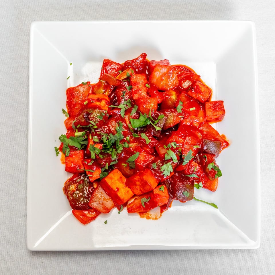 Saucy roasted vegetables, including peppers and onions, garnished with fresh cilantro on a white square plate.