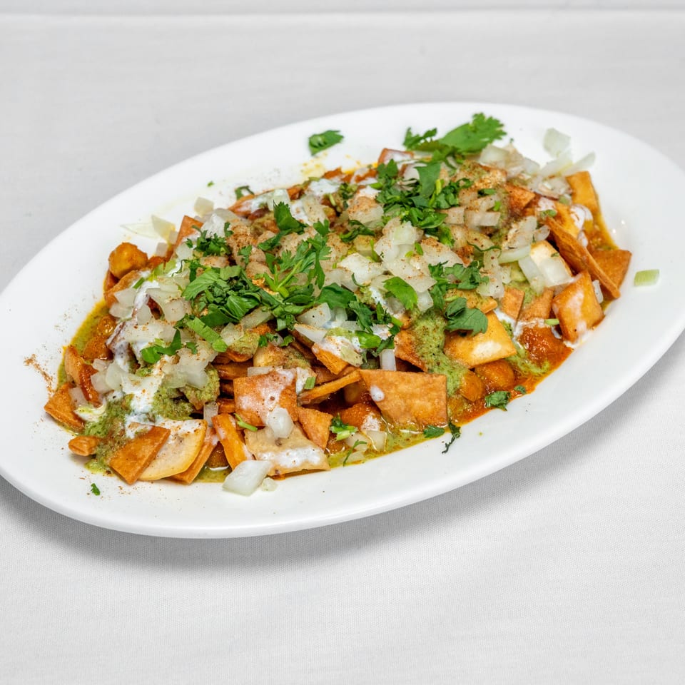 Crispy tortilla chips topped with diced onions, chopped cilantro, green sauce, white crema, and reddish salsa on a white platter.