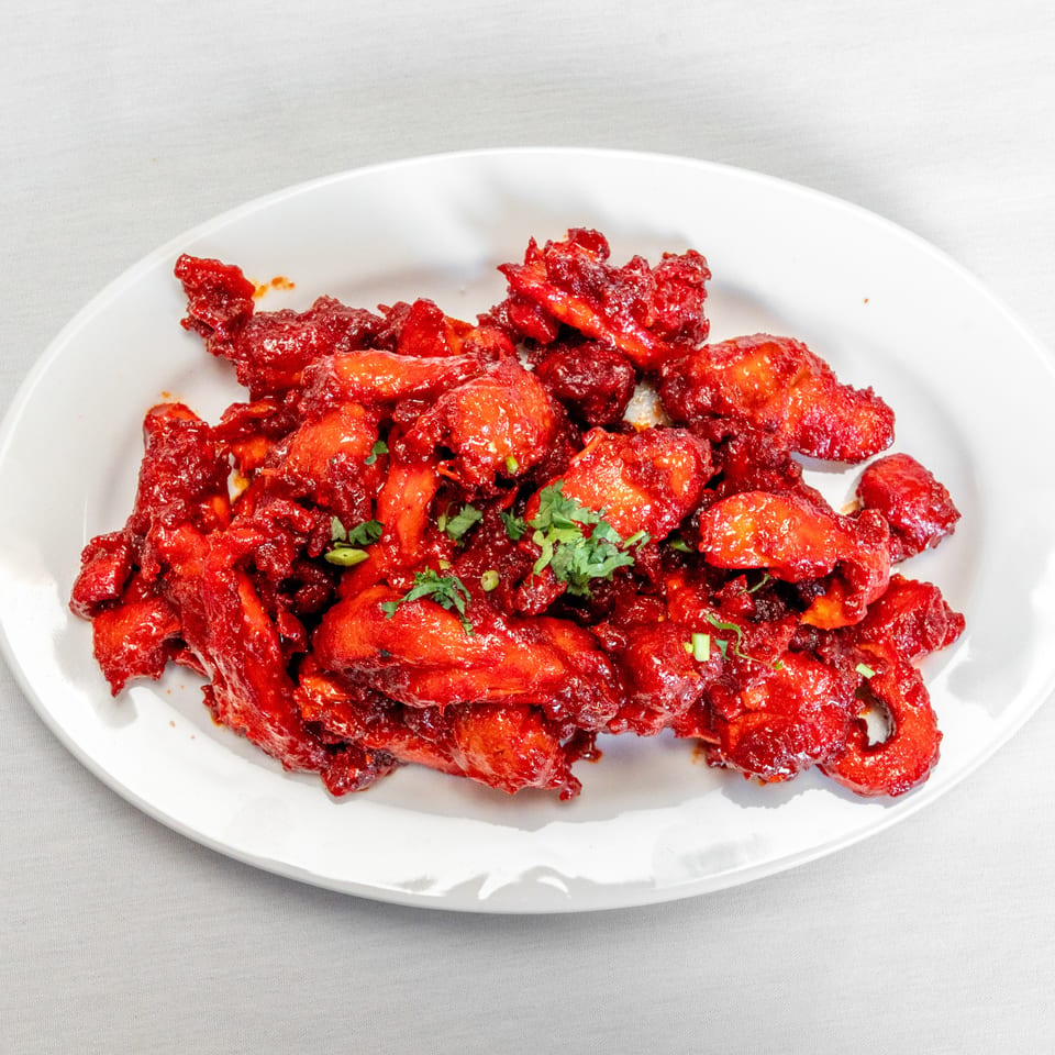 A white plate holds red-sauced fried chicken pieces garnished with chopped green herbs.