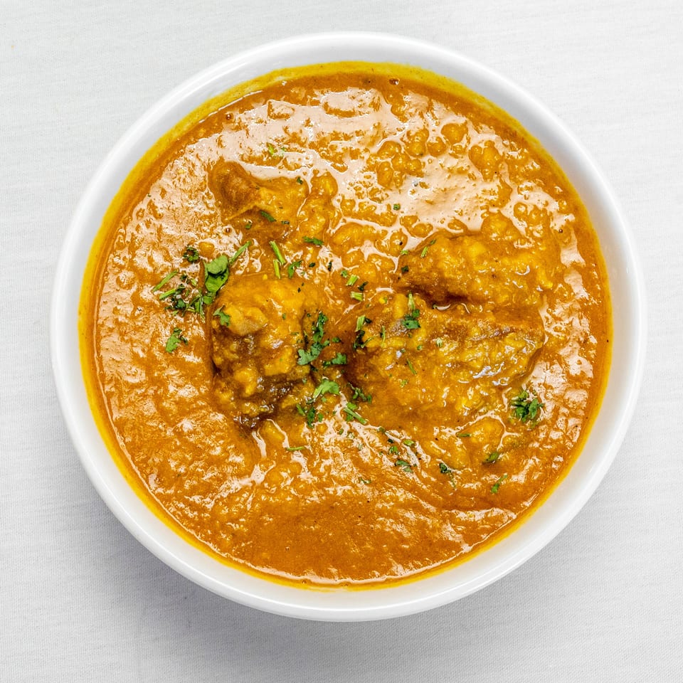 Top-down view of a white bowl filled with rich orange curry, garnished with chopped cilantro.