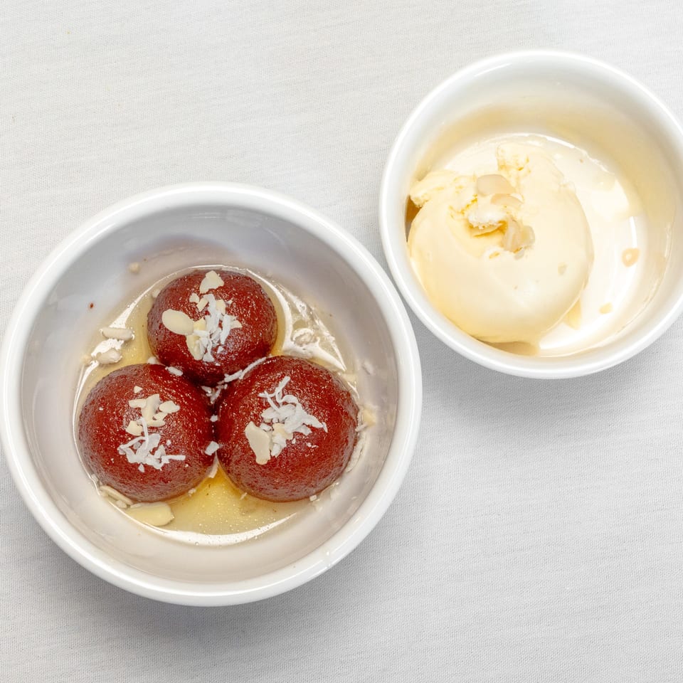 Three syrup-soaked gulab jamun topped with almond flakes beside vanilla ice cream in white bowls.
