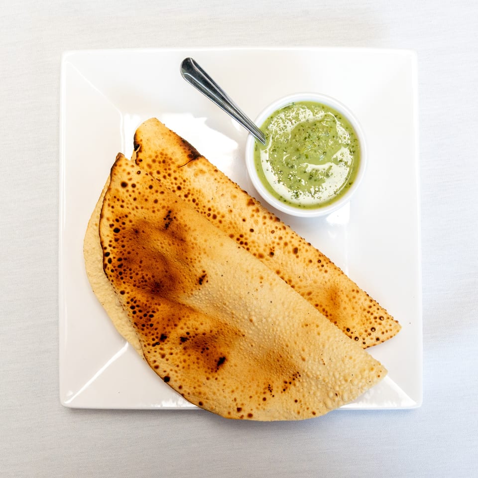Crispy triangular flatbreads arranged on a white plate with a bowl of green dipping sauce and a spoon.