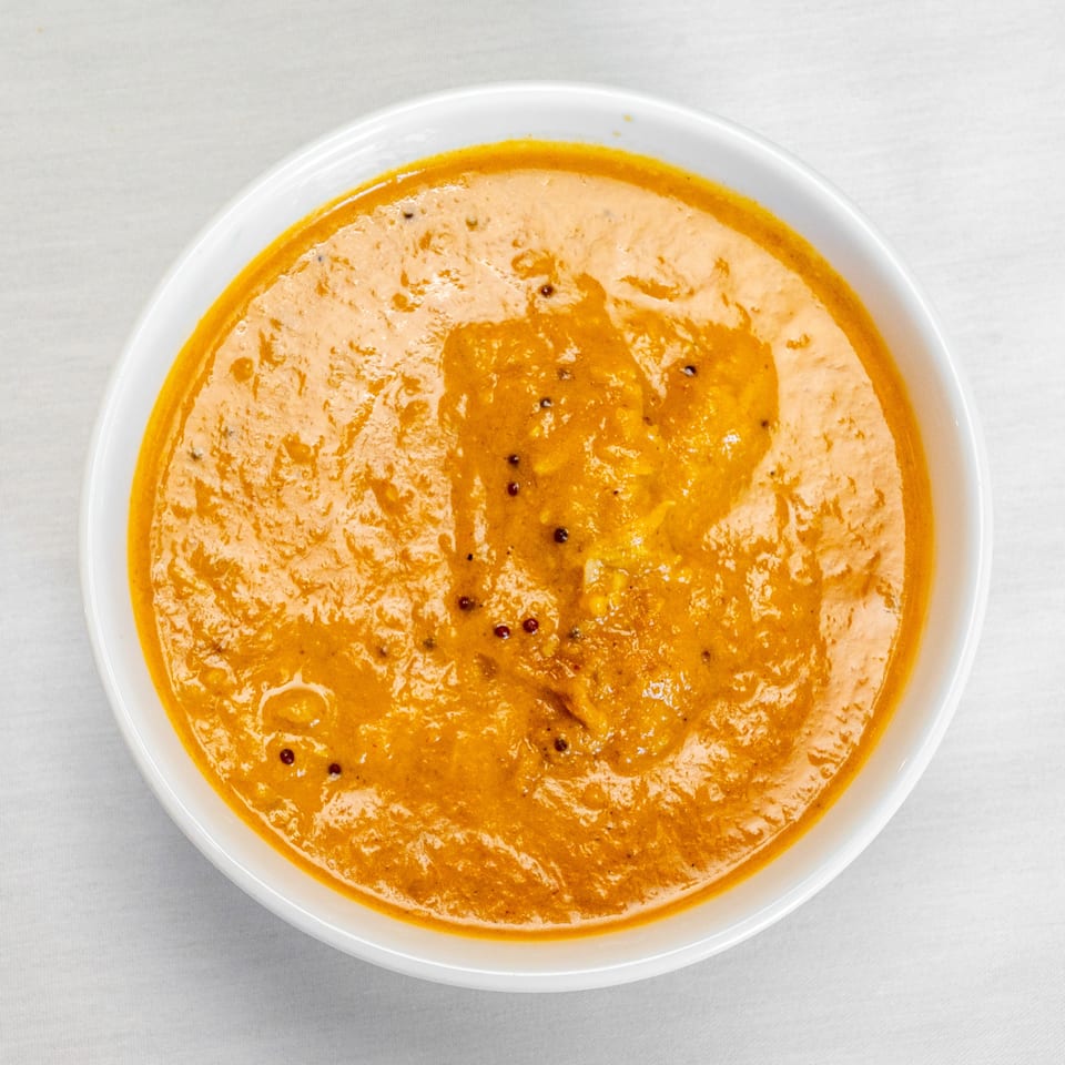 Top-down view of creamy orange curry garnished with dark spices in a white bowl.