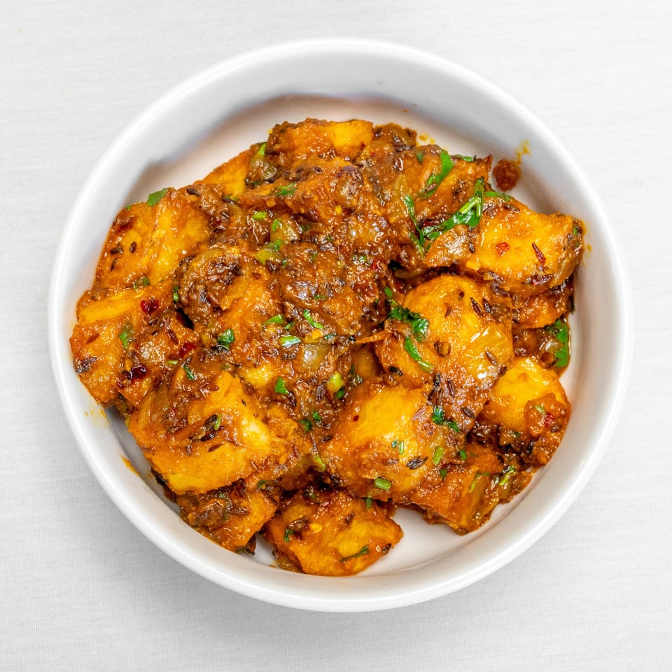 Bowl of golden spiced potato chunks garnished with fresh herbs and chili flakes.