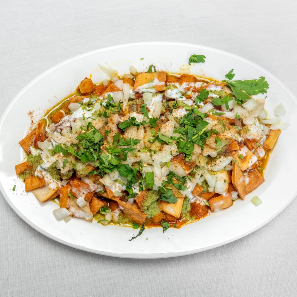 Crispy tortilla chips topped with yogurt, chutney, diced onions, spices, and fresh cilantro on a white platter.