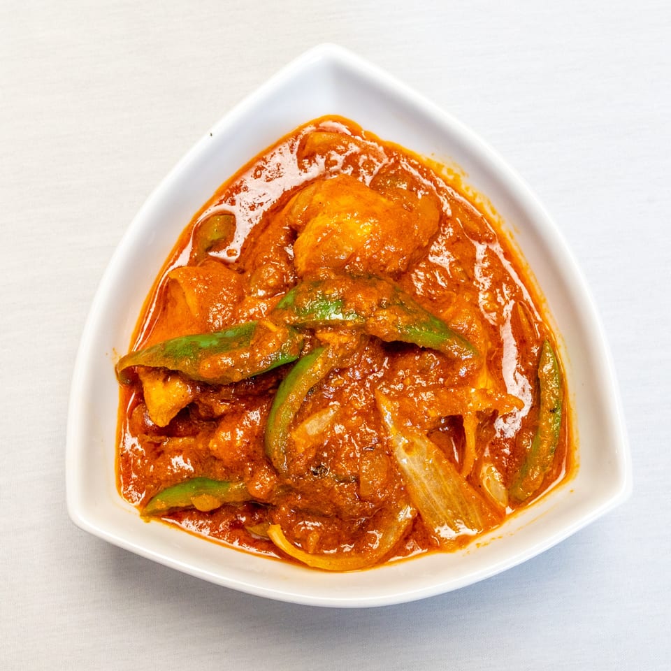 Creamy red curry with chicken, green peppers, and onions served in a white bowl.