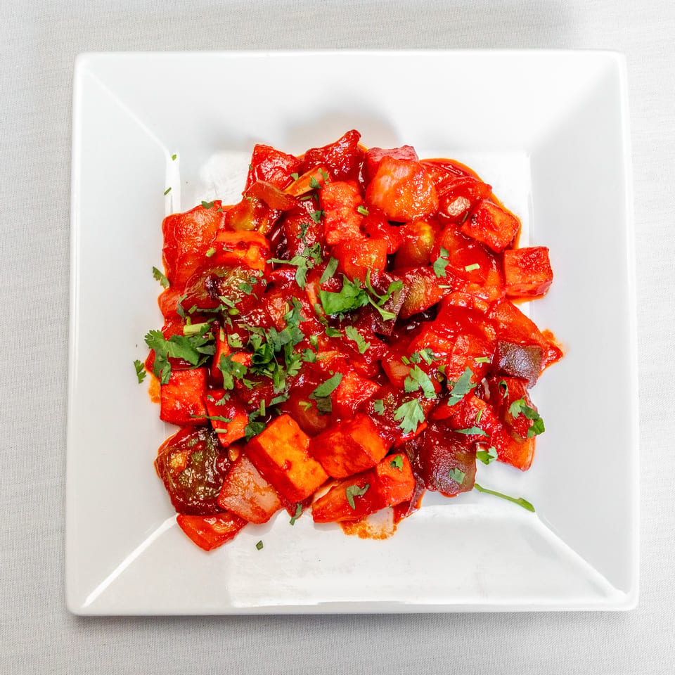 Red-sauced mixed vegetables topped with fresh cilantro, served on a white square plate.