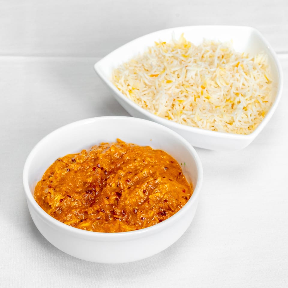 A bowl of spicy orange curry sits beside a bowl of seasoned basmati rice on a white tablecloth.
